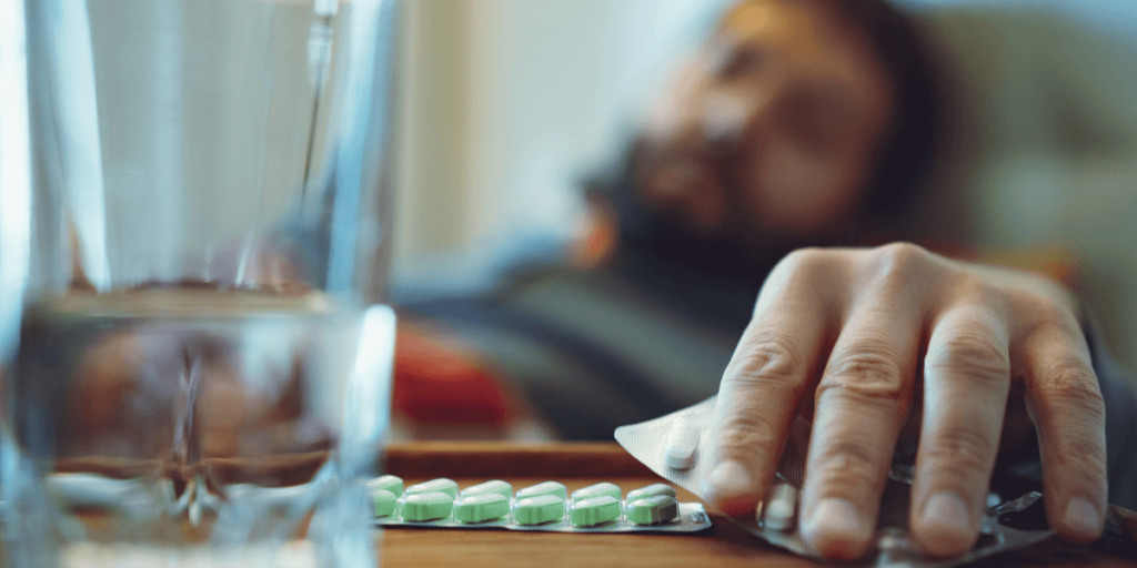 Man reaching out to take a medicine tablet from the table.