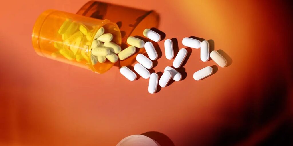 Prescription bottle tipped over with yellow and white painkiller tablets spilled on an orange surface